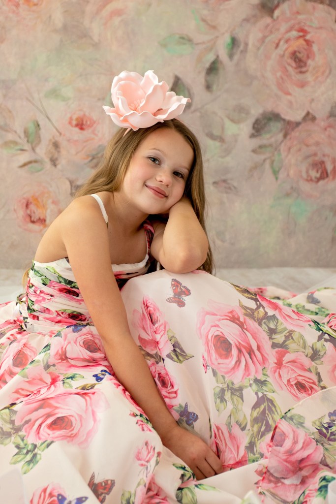 Smiling preteen girl wearing a dress with roses and butterflies and a floral headpiece in her child portrait session.